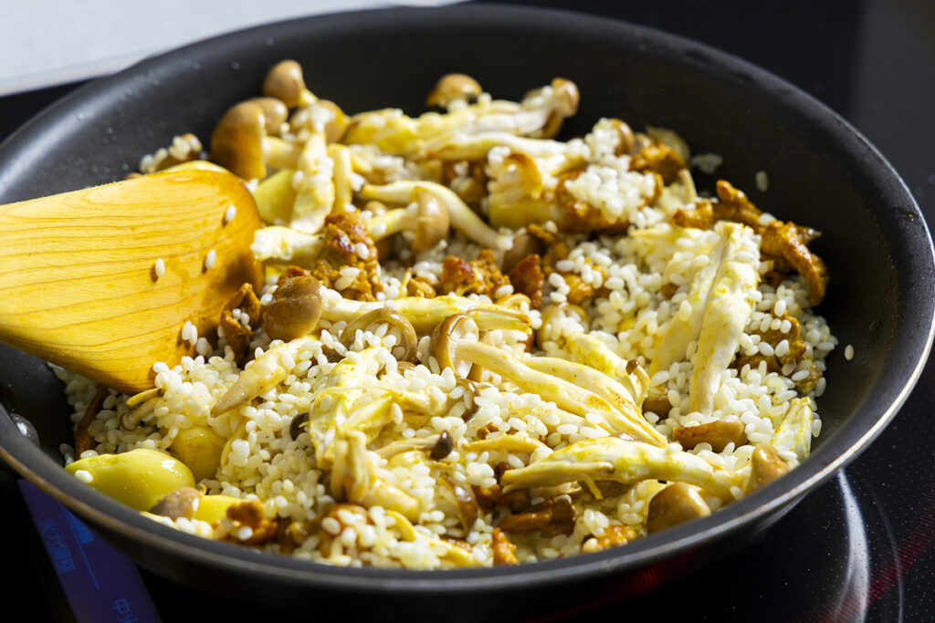 ニンニクの香りが立ったら、豚肉、シメジを加え、さらに水を切ったコメを入れて混ぜる。